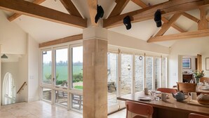 A spacious dining area with a view of the outdoors, wooden beams, and a table set for dining. - Blackhill barn - in the heart of the Cotswolds (Craswall)