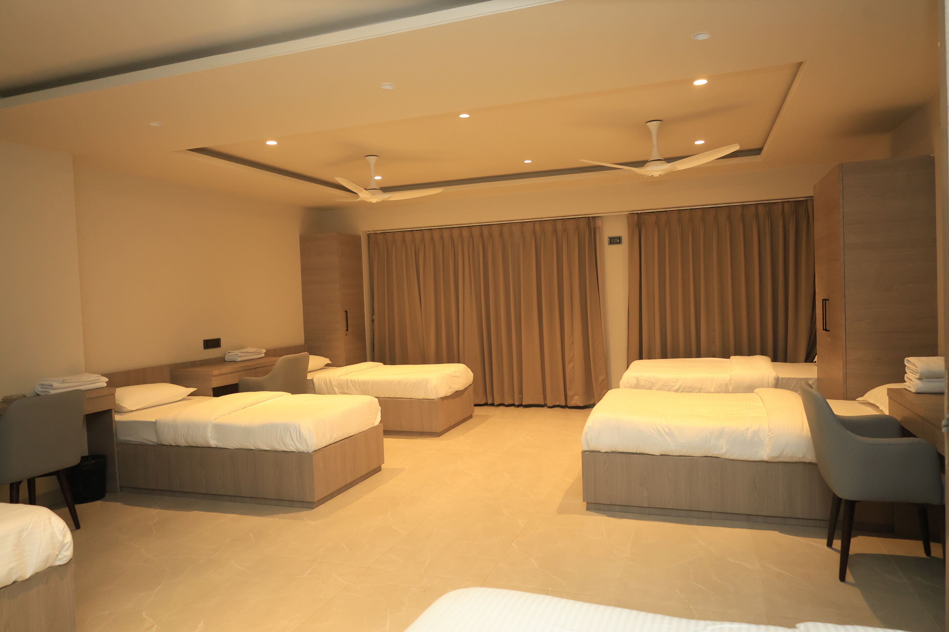 A hotel room with two beds, a desk, a chair, and a ceiling fan.