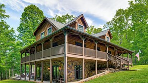 A two-story log cabin with a balcony, stone foundation, and an American flag. - Hot Tub & Patio: Bedford Log Cabin on 10 Acres! (Bedford)
