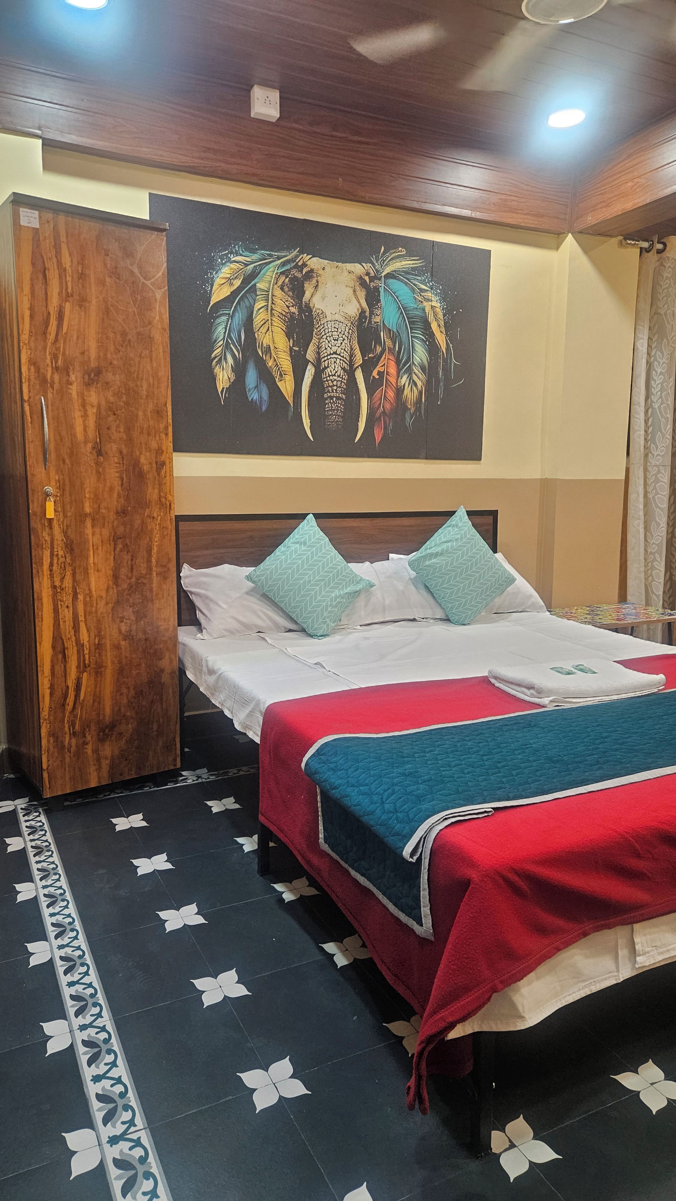 A hotel room with a bed, pillows, a blanket, a wall with a painting, and a patterned floor.