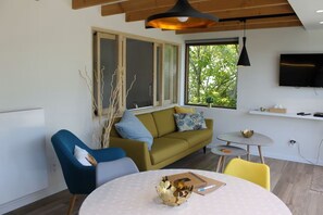 Ein modernes Wohnzimmer mit einer Couch, Sesseln, einem kleinen Tisch und einem an der Wand befestigten Fernseher.