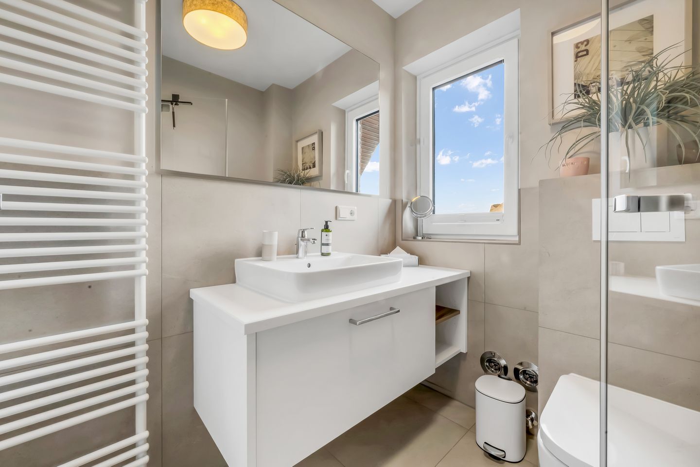 A modern bathroom with a large mirror, a window, a sink, and a toilet.