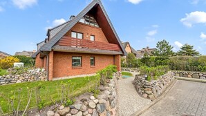 A modern house with a sloped roof, brick exterior, and a stone pathway leading to the entrance. - Küstenkoje - Modern 3-room vacation apartment with approx. 55 m² living space, for up to (Wenningstedt-Braderup (Sylt))