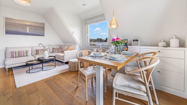 A modern loft apartment with a dining area, a sofa set, a kitchen, and a large window with a city view. - Küstenkoje - Modern 3-room vacation apartment with approx. 55 m² living space, for up to (Wenningstedt-Braderup (Sylt))