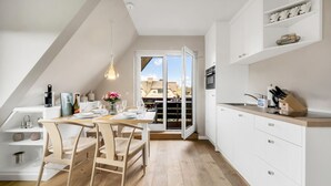 A modern kitchen with a dining area, white cabinetry, and a view through a glass door. - Küstenkoje - Modern 3-room vacation apartment with approx. 55 m² living space, for up to (Wenningstedt-Braderup (Sylt))