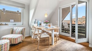 A dining area with a table set for two, a chair, and a sofa with a chevron pattern. - Küstenkoje - Modern 3-room vacation apartment with approx. 55 m² living space, for up to (Wenningstedt-Braderup (Sylt))