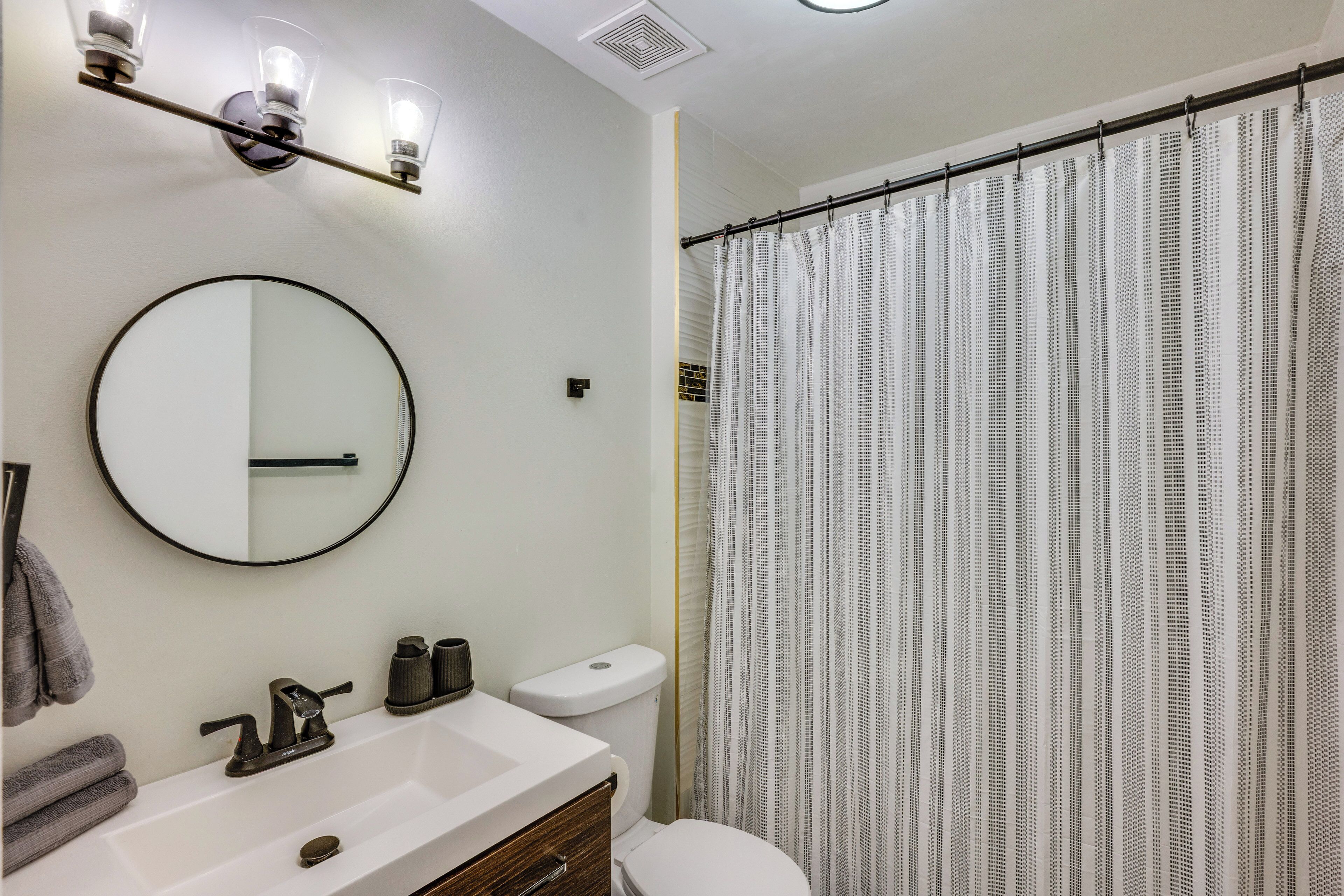 A bathroom with a round mirror, a white sink, a toilet, and a shower curtain.