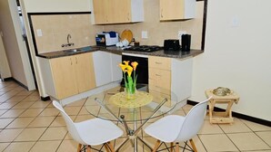 Une cuisine compacte avec une table à manger en verre, des chaises blanches et un petit tabouret en bois.