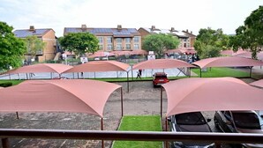 Un espace de stationnement comprenant plusieurs places de parking couvertes et, en arrière-plan, un bâtiment équipé de panneaux solaires.