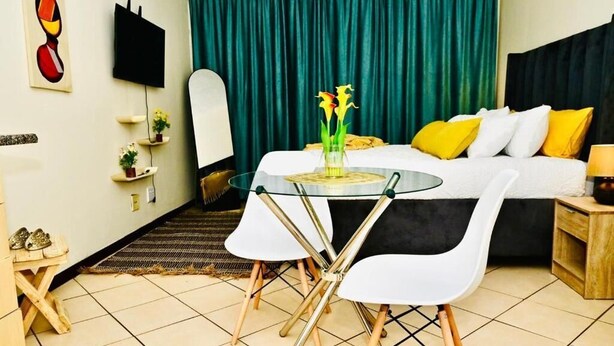 Une chambre d’hôtel avec un lit, une télévision, une table en verre avec des chaises et une petite table où sont posées des chaussures.