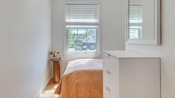 Un dormitorio con una cama, un aparador, una mesita redonda de madera y una ventana con persianas.