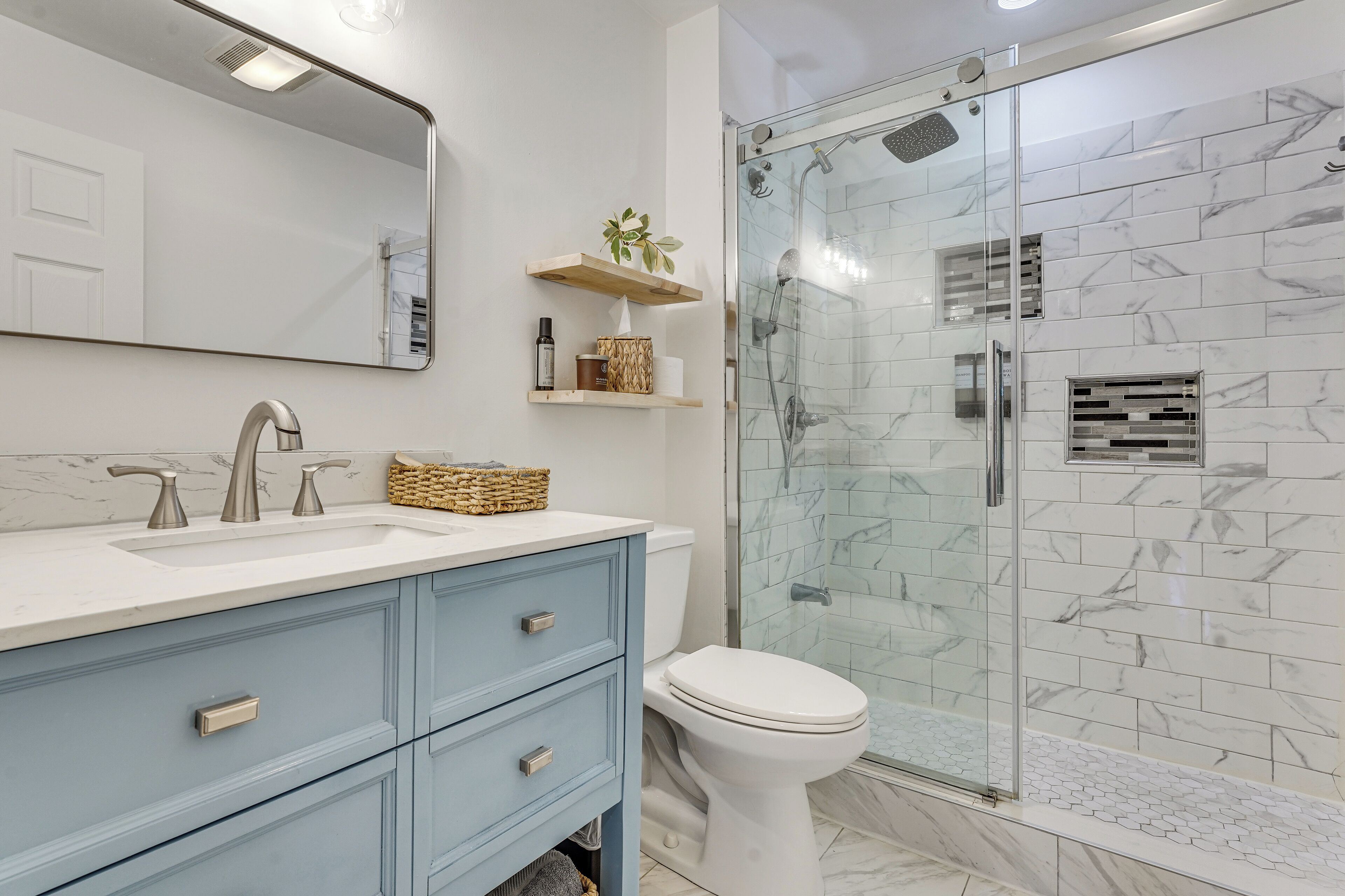 A bathroom with a glass-enclosed shower, a white toilet, a blue vanity with drawers, and a large mirror.