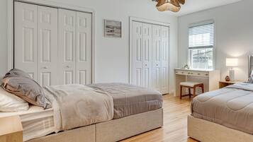 A bedroom with two beds, a desk, and a window.