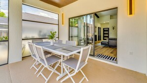 Un patio exterior moderno con una mesa, sillas, una planta en maceta y un ventanal corredero que da a un espacio interior.