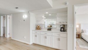 A modern kitchen with white cabinetry, a large mirror, and a coffee machine. - Stunning Views, Luxe Decor: Suntide III - Unit 805 (South Padre Island)