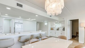 A modern kitchen with a marble island, bar stools, and a dining table. - Stunning Views, Luxe Decor: Suntide III - Unit 805 (South Padre Island)