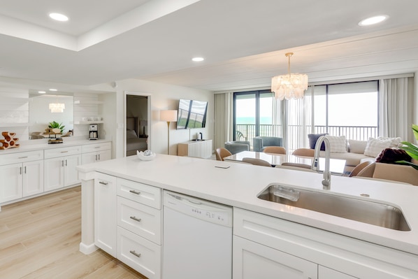 A modern kitchen with a dishwasher, a dining area with a table and chairs, and a view of the ocean through large windows. - Stunning Views, Luxe Decor: Suntide III - Unit 805 (South Padre Island)
