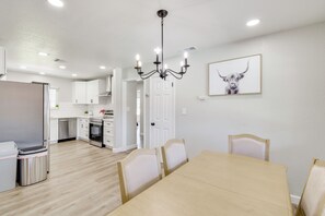 Een moderne keuken met witte kastjes, een eethoek met een tafel en stoelen, en een kroonluchter.