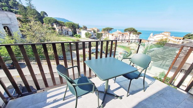 Un balcón con mesa y sillas, con vista a una zona costera con edificios y cielo despejado.