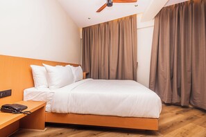 A hotel room with a bed, wooden headboard, a desk with a telephone, and a ceiling fan.