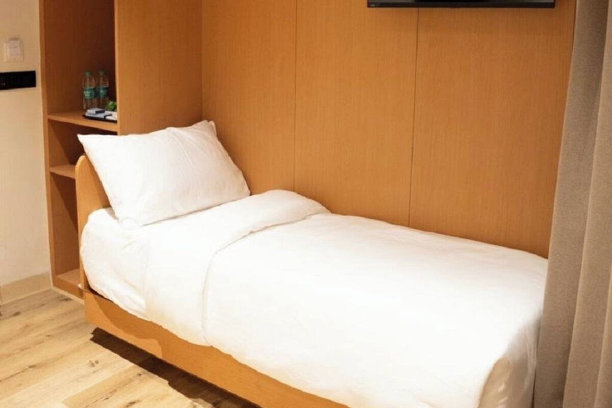 Ein Einzelbett mit Kopfteil, ein Flachbildfernseher an der Wand und ein Holzschrank.