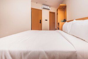 A hotel room with a bed, wooden doors, an air conditioning unit, and a small shelf with toiletries.
