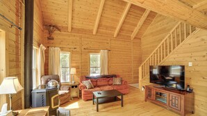 Interior de una cabaña de madera con sofá, televisión y chimenea.