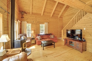 A wooden cabin interior with a sofa, television, and a fireplace.
