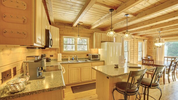 Interior de una cabaña de madera con cocina, comedor y asientos de bar.