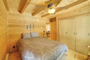 Une chambre dans une cabane en bois, avec un lit, un ventilateur de plafond et une armoire.