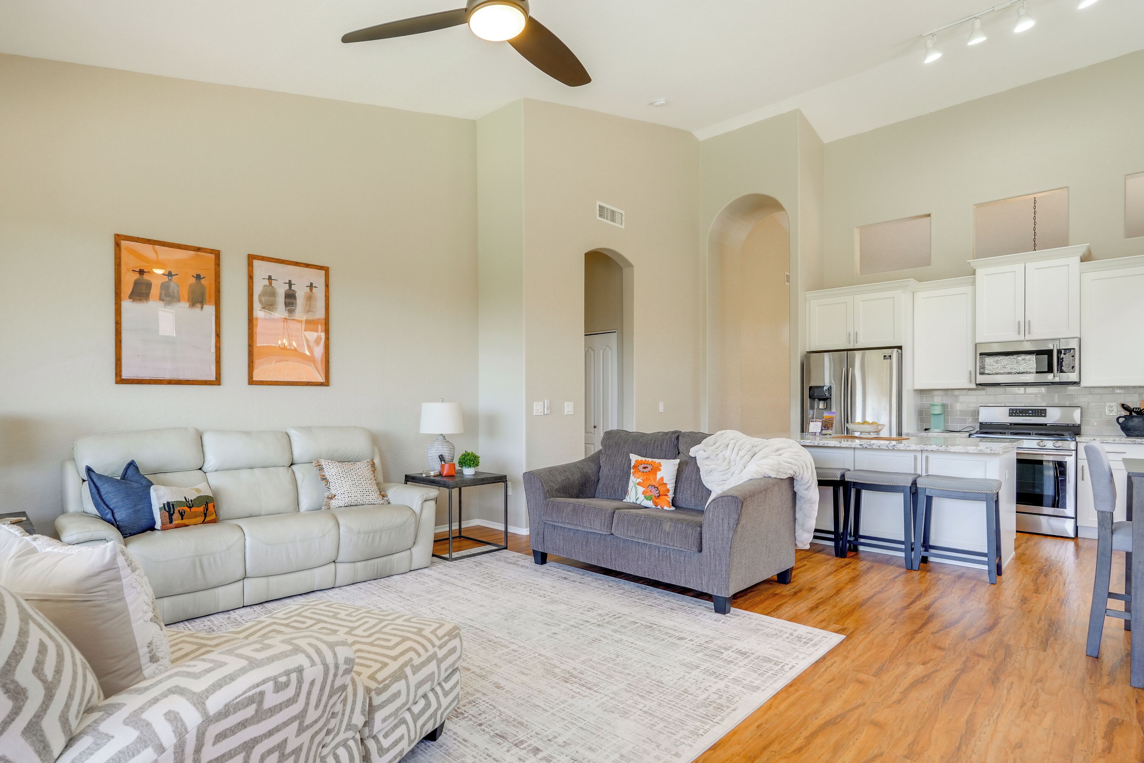 A modern living room with a grey sofa, a patterned ottoman, and a ceiling fan.