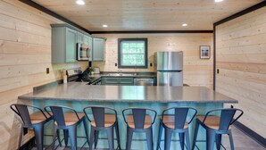 A kitchen with wooden walls, a central island with bar stools, stainless steel appliances, and a window. - Walk to Kentucky Lake! Pet-Friendly Murray Duplex (Murray)