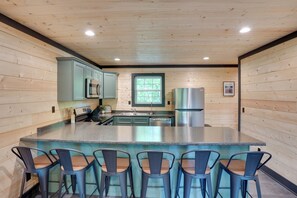 Une cuisine aux murs en bois, avec un îlot central doté de tabourets, des appareils en acier inoxydable et une fenêtre.