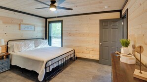 Un dormitorio con cama, una mesita de noche, un escritorio con planta, una puerta y un ventilador de techo.