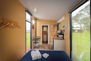 A hotel room with a bed, a desk with a computer, a small kitchenette, and a view of the outdoors. - Lara Grove Cottage 1 by Tiny Away (Purdeet)