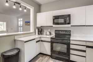 A kitchen with white cabinets, a black microwave, a stove, and a trash can.