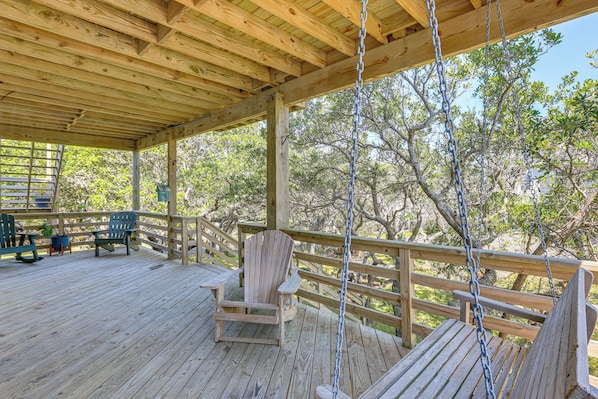 A wooden deck with a swing, chairs, and a view of trees.