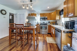 A kitchen with wooden cabinets, stainless steel appliances, a dining table with chairs, and a water dispenser. - Dog-Friendly Home w/ Dock & Views on Waneta Lake! (Wayne)