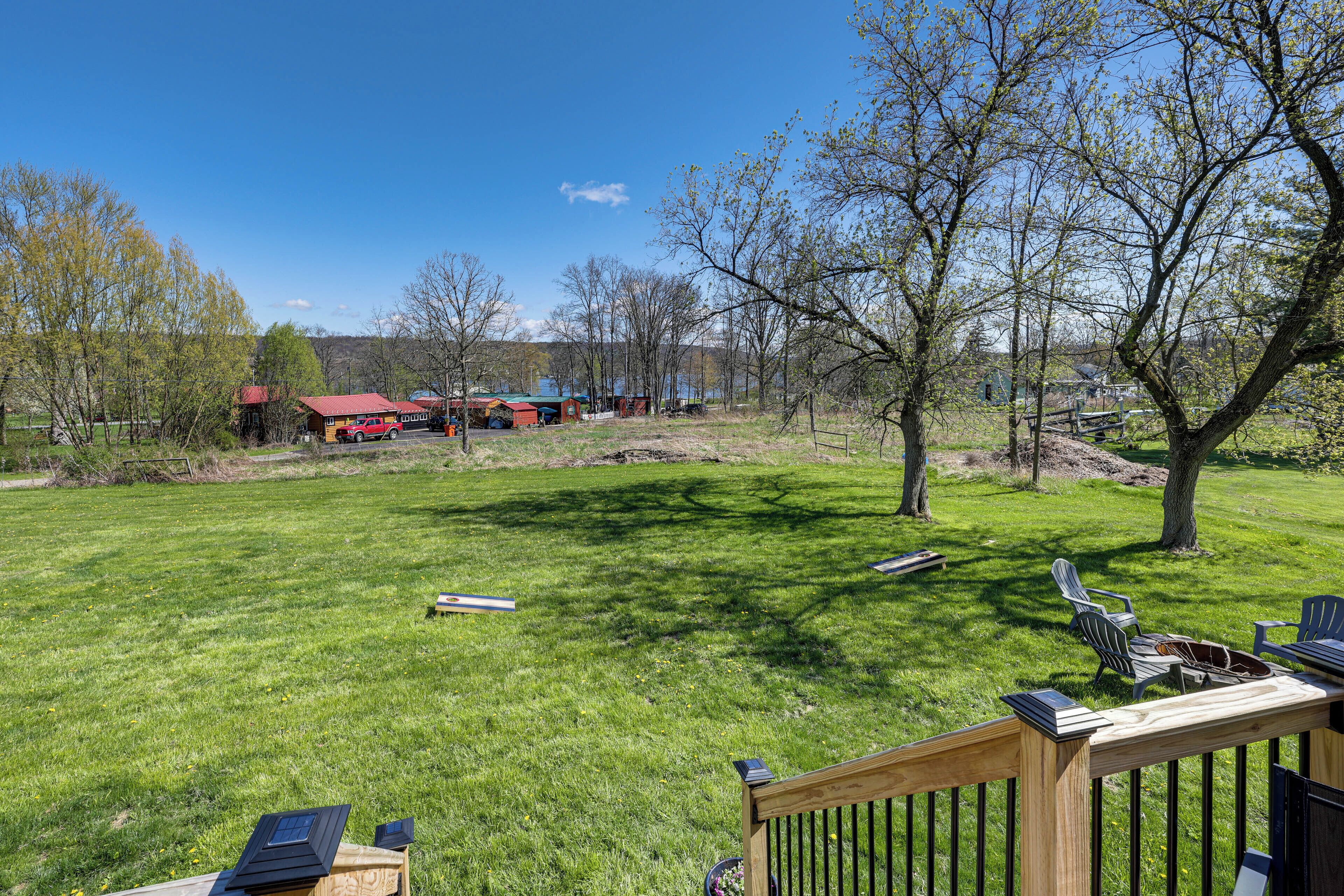A grassy backyard with a wooden deck, a red barn, and a clear blue sky.