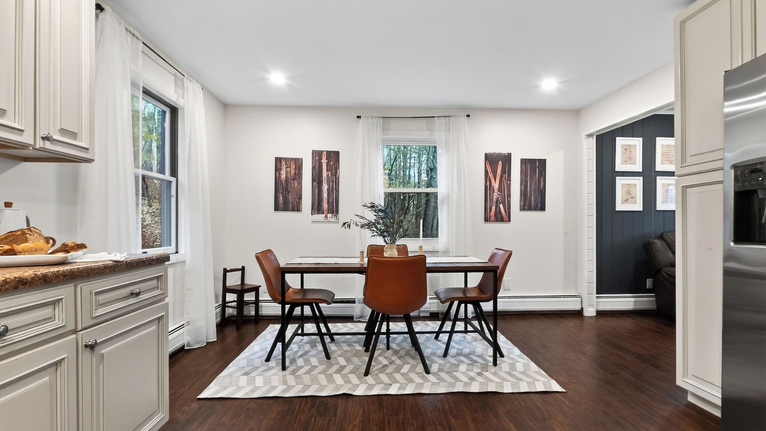 A kitchen with a dining area, white cabinetry, a refrigerator, and a window with a view of trees.