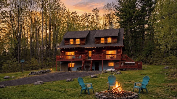 A cabin with a deck, a fire pit, and two chairs.