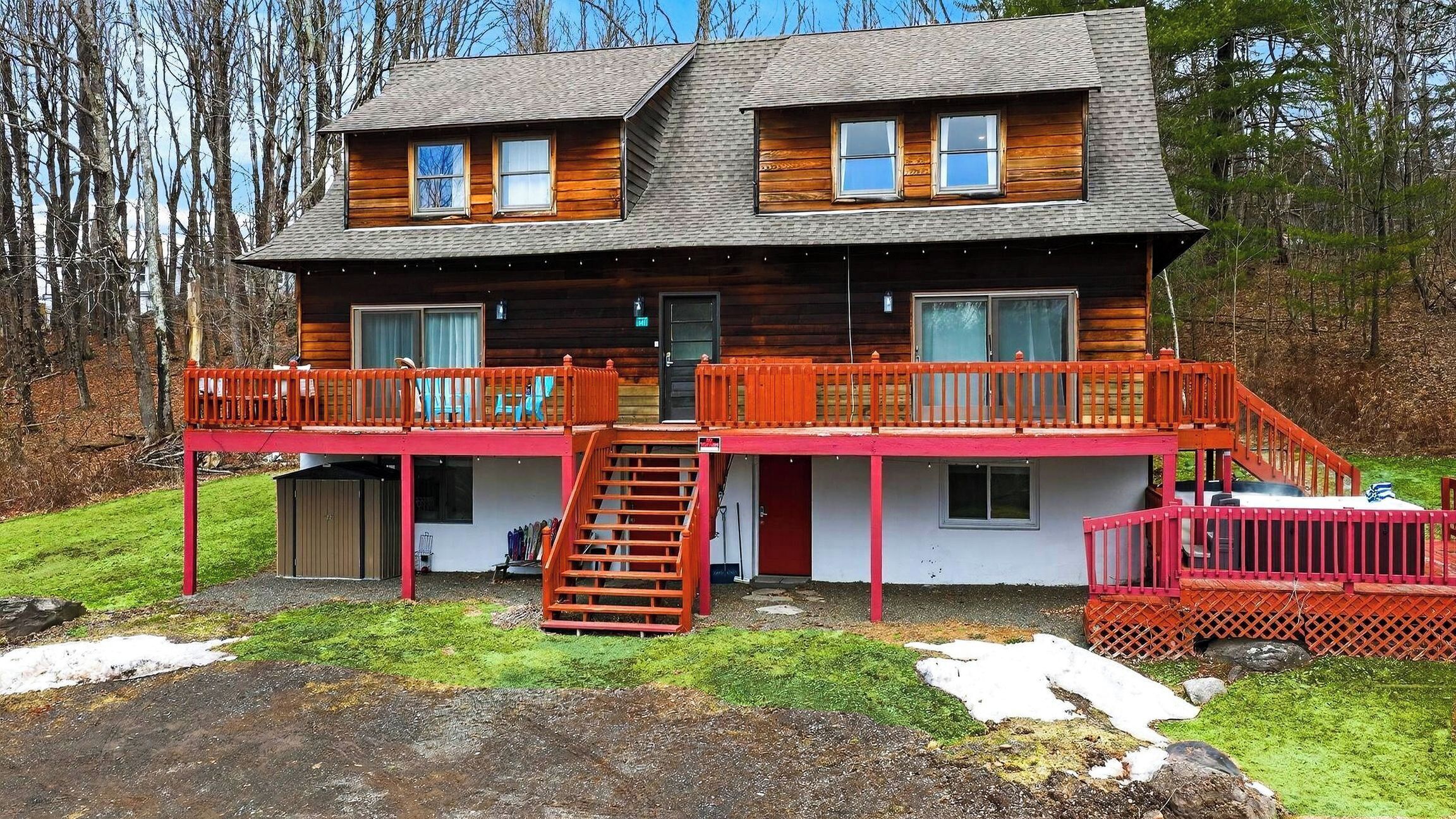 A two-story log cabin with a red balcony and a small porch area.