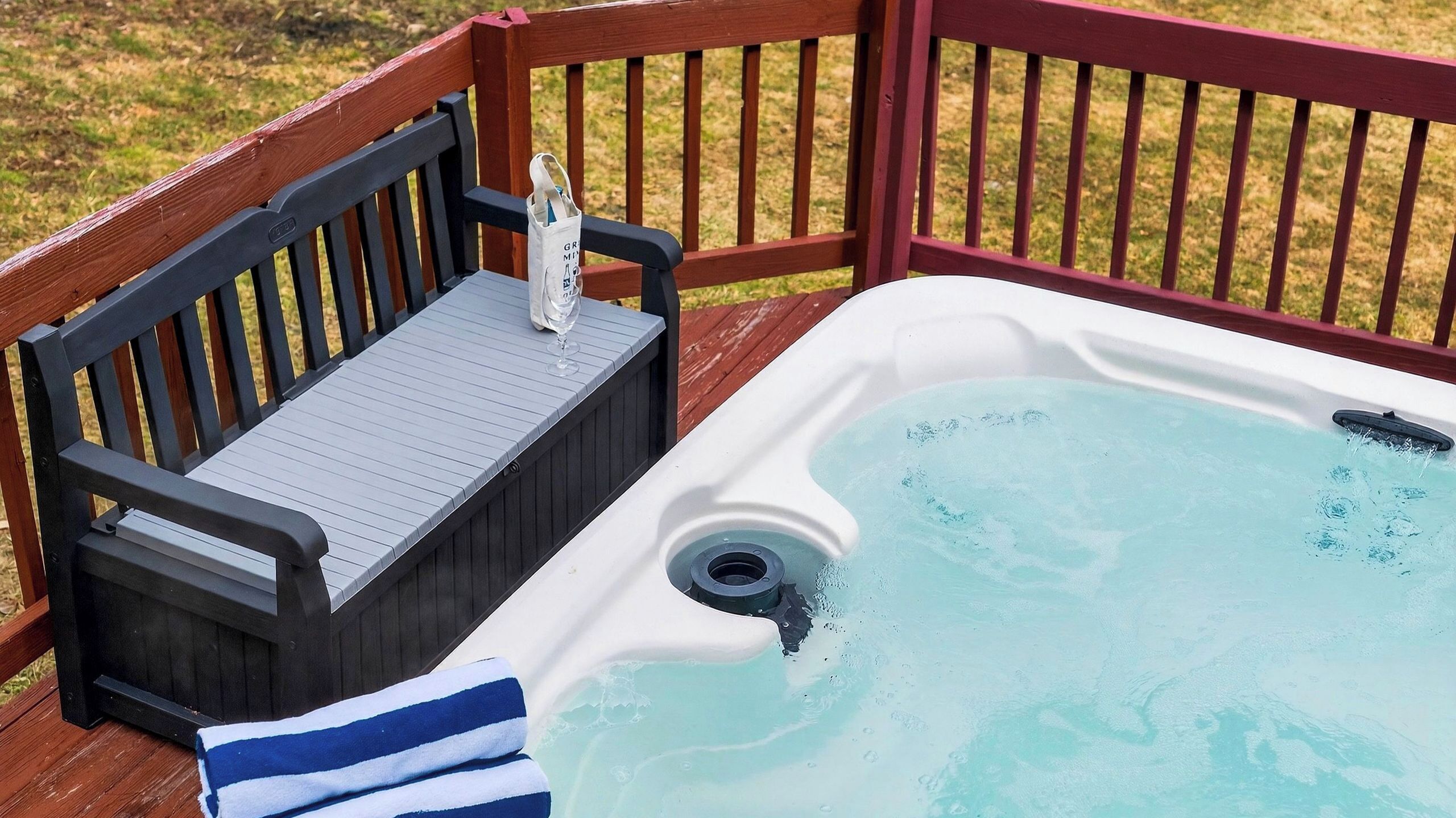 A hot tub with a wooden deck, a bench, and a towel.