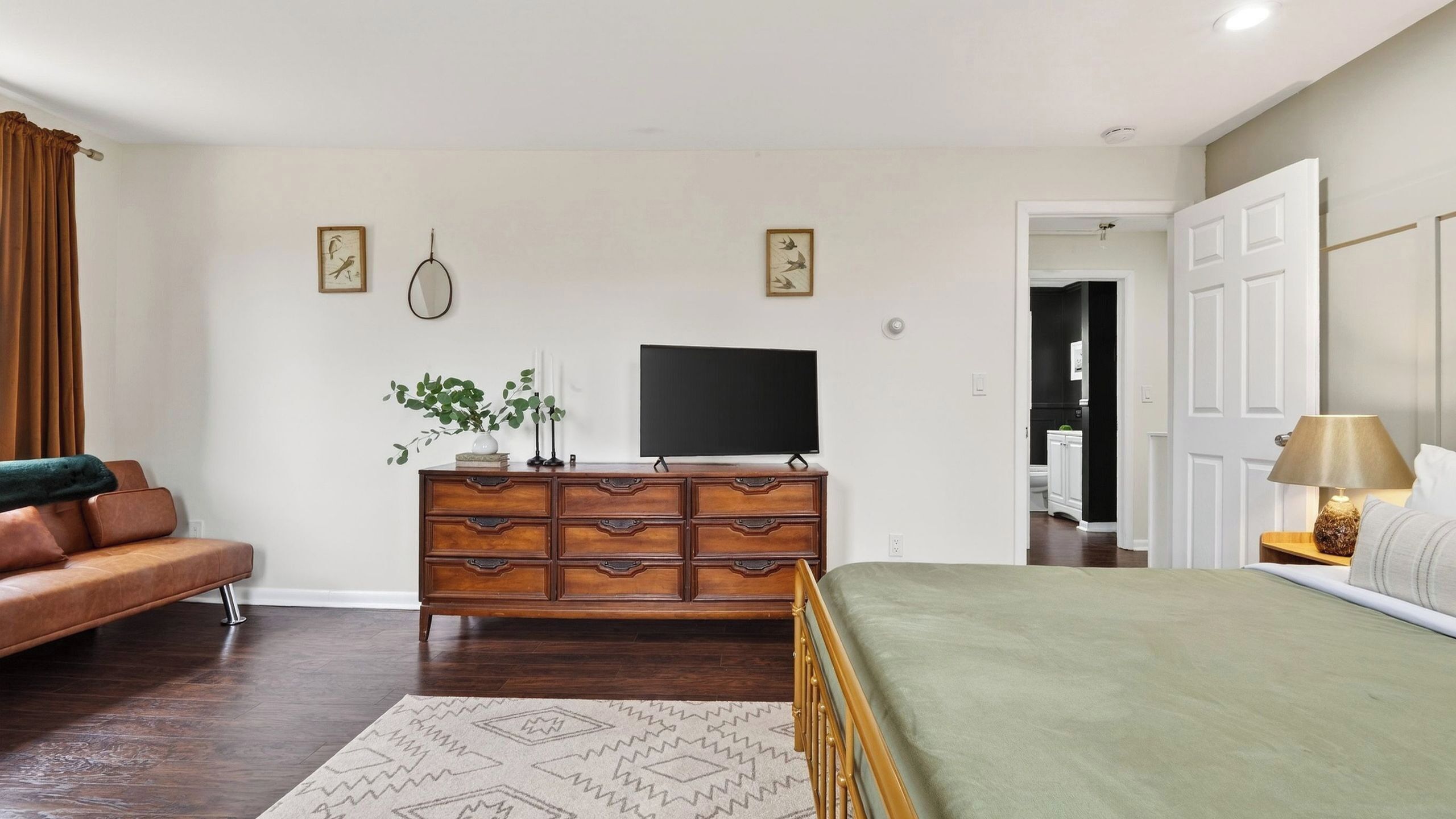 Quarto com cama, penteadeira, televisão, sofá e porta que dá para um banheiro.