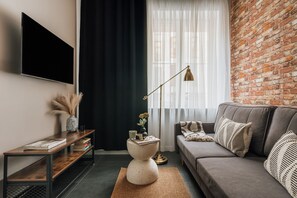 Ein modernes Wohnzimmer mit Backsteinwand, grauem Sofa, Couchtisch, Wand-Fernseher und Stehlampe.