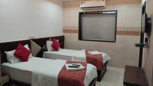Ein Hotelzimmer mit zwei Betten, einem Deckenventilator, einer Klimaanlage, einem Fernseher und einem kleinen Tisch.