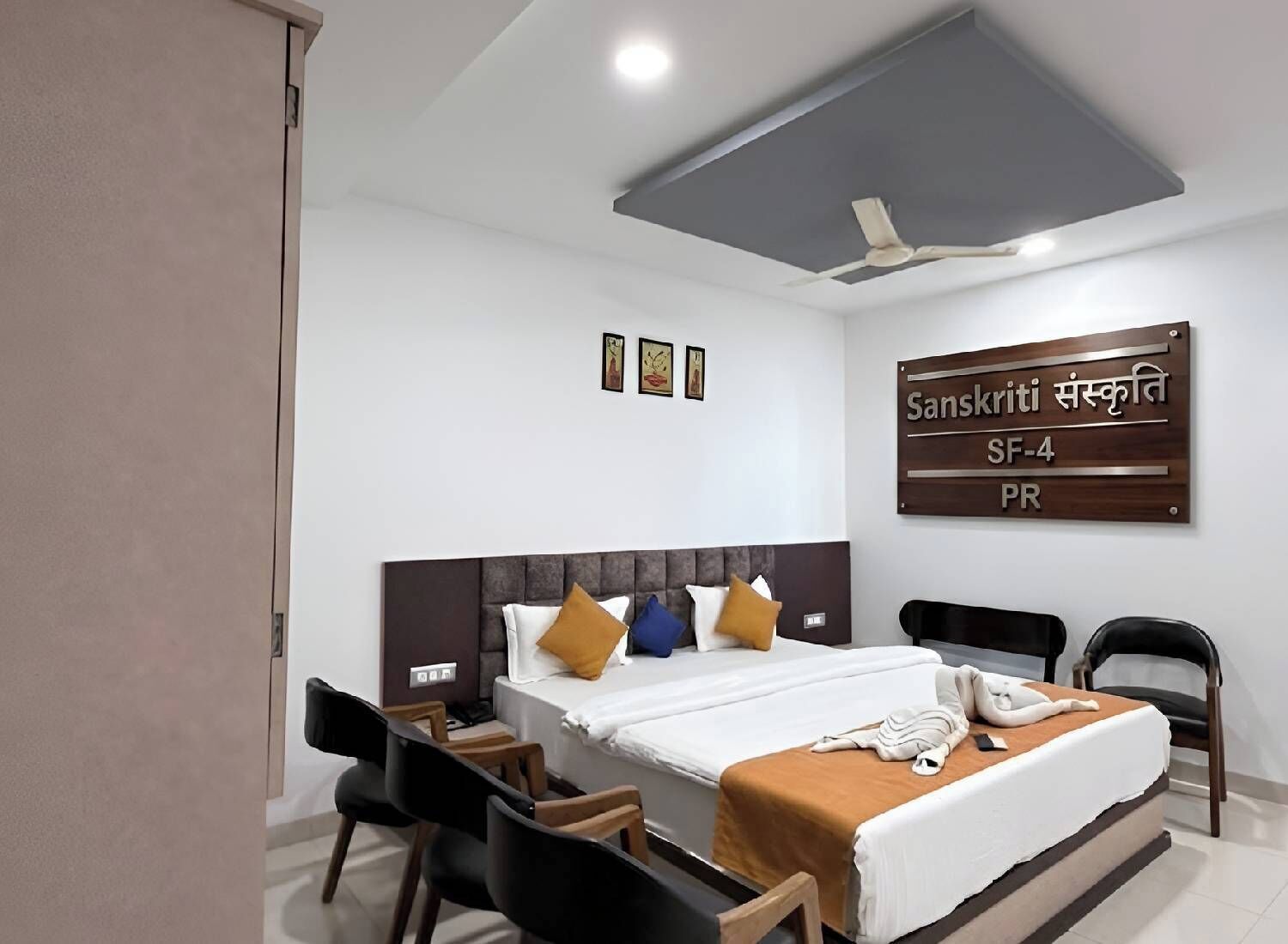 A hotel room with a bed, chairs, a desk, a ceiling fan, and a sign indicating room number SF-4.