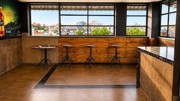 Interior de un restaurante con barra, ventanales y vista a la ciudad.