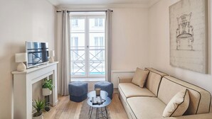 A living room with a sofa, ottomans, a fireplace, a television, and a large window. - Lovely apartment with AC - Center of Paris (Paris)