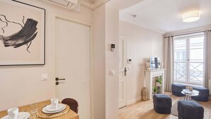 A modern living room with a fireplace, a dining area with a table set for two, and a large window with curtains. - Lovely apartment with AC - Center of Paris (Paris)